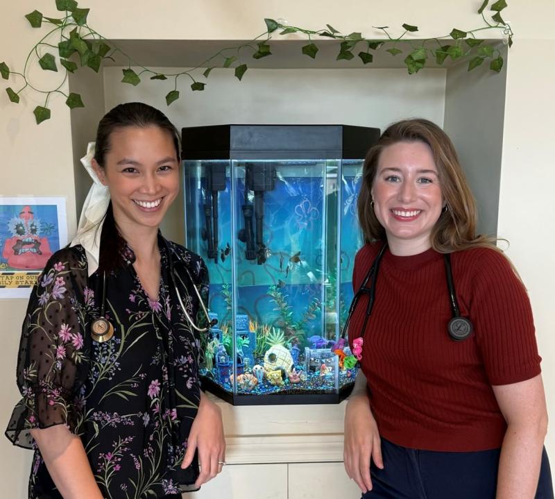 two women smiling in front of a fish tank
